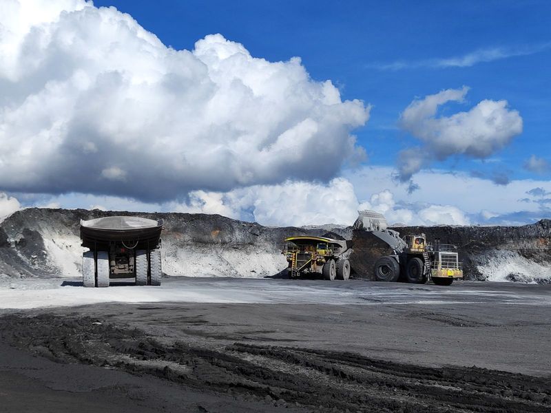 Haul trucks working in a large open-pit coal mine under a blue sky