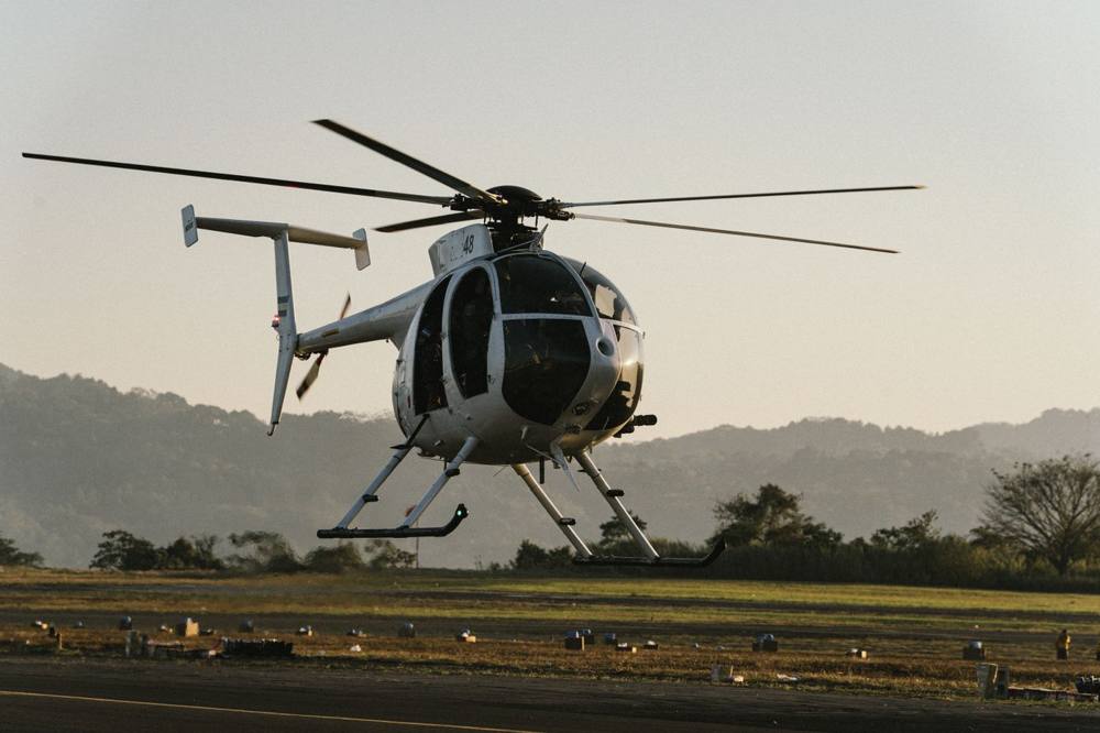 A light helicopter lifting off from an airfield at sunrise