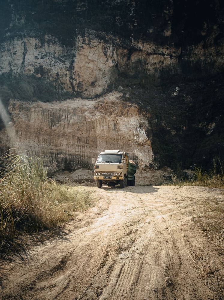 A truck on a dusty haul road beside a quarry face